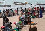 Im Wasser viele Boote, am Land Männer und Frauen, die mit ihren großen Bottichen am Land auf den Fisch warten