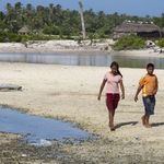 An einem Strand gehen zwei junge Menschen entlang, sie sind umgeben von großen Pfützen