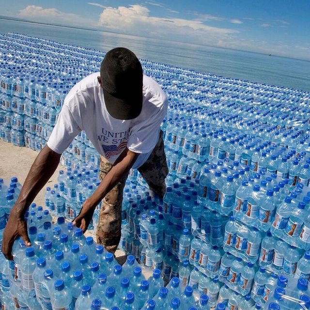 Jede Menge Wasserflaschen des UN-Welternährungsprogramm (WFP) Ein Mann sortiert hunderte Wasserflaschen, im Hintergrund sieht man das Meer.