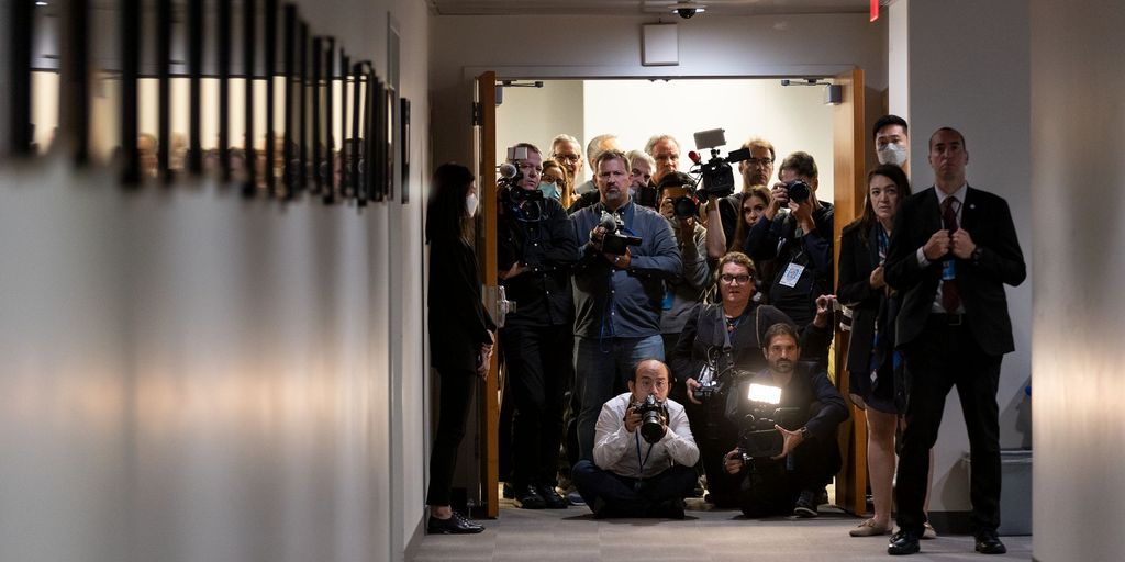 Eine Gruppe Journalistinnen und Journalisten sitzt und steht am Ende eines schmalen Gangs mit vielen Fotoapparaten in den Händen und schaut ernst Richtung Kamera.